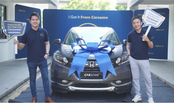 Founders holding carsome buy car signages with a car wrapped in blue ribbon in between